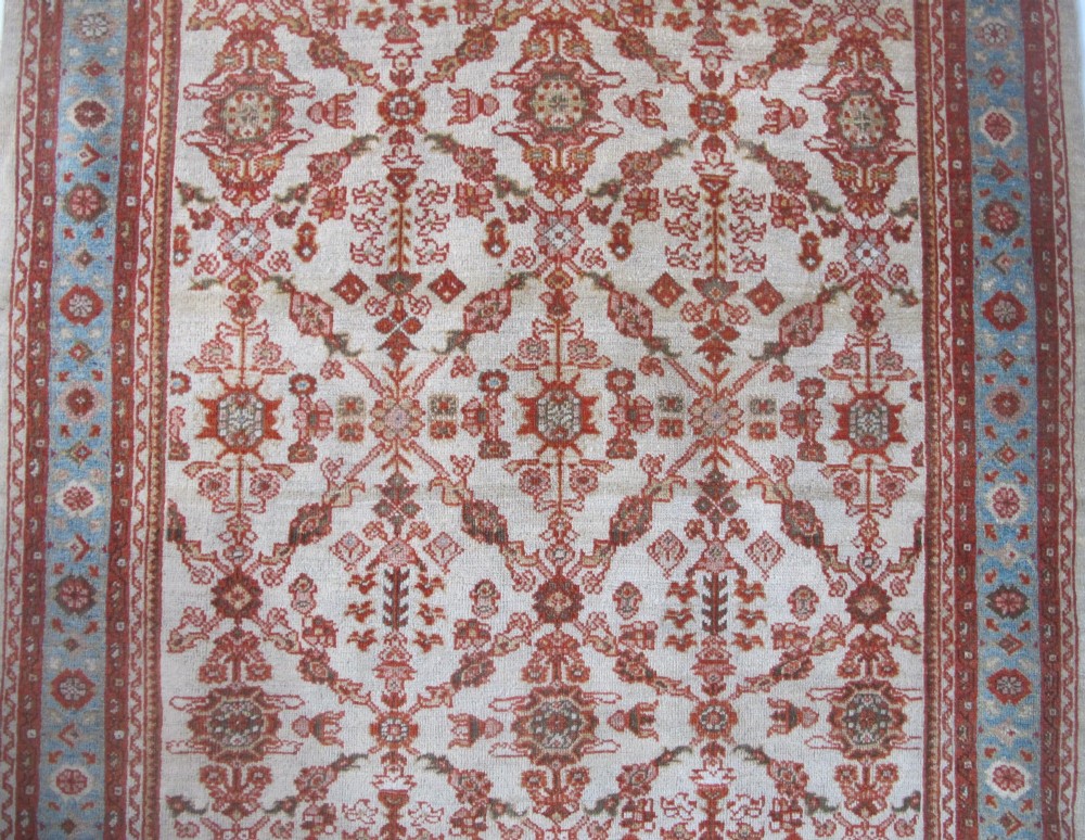 An antique Persian Ziegler wool rug featuring a repeating soft terracotta and light blue floral pattern across an ivory field, bordered by a decorative floral band. View II