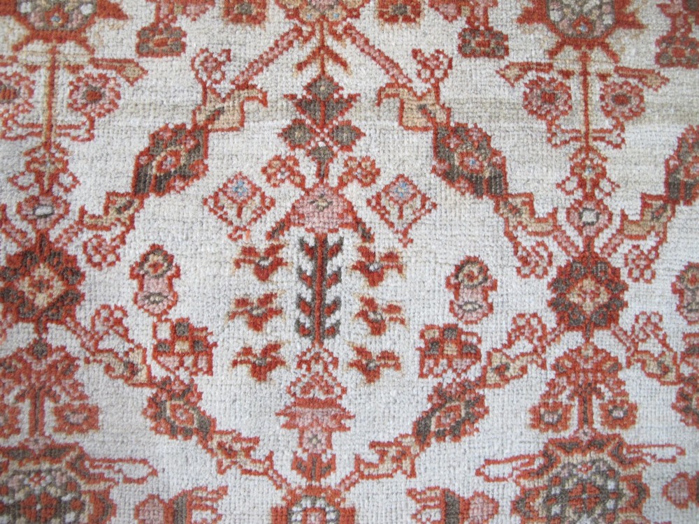 An antique Persian Ziegler wool rug featuring a repeating soft terracotta and light blue floral pattern across an ivory field, bordered by a decorative floral band. View III