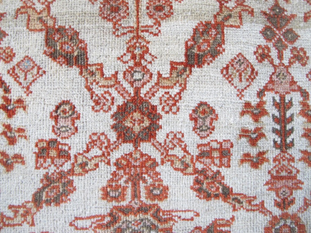 An antique Persian Ziegler wool rug featuring a repeating soft terracotta and light blue floral pattern across an ivory field, bordered by a decorative floral band. View IV