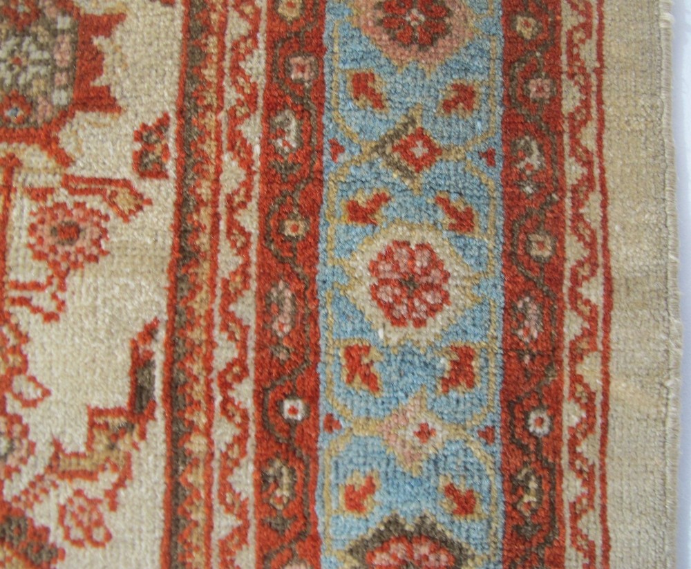 An antique Persian Ziegler wool rug featuring a repeating soft terracotta and light blue floral pattern across an ivory field, bordered by a decorative floral band. View V