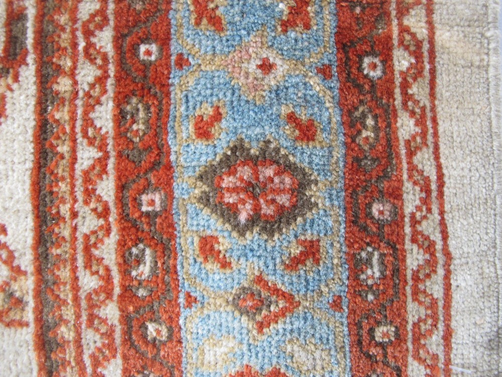 An antique Persian Ziegler wool rug featuring a repeating soft terracotta and light blue floral pattern across an ivory field, bordered by a decorative floral band. View VI