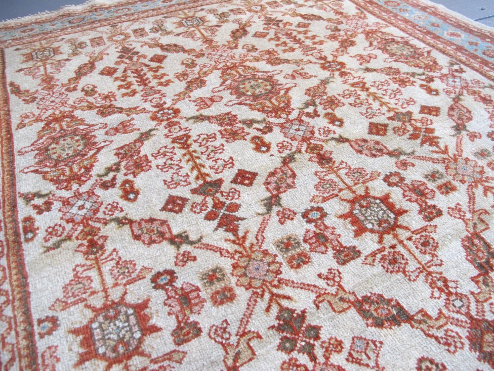 An antique Persian Ziegler wool rug featuring a repeating soft terracotta and light blue floral pattern across an ivory field, bordered by a decorative floral band. View IX