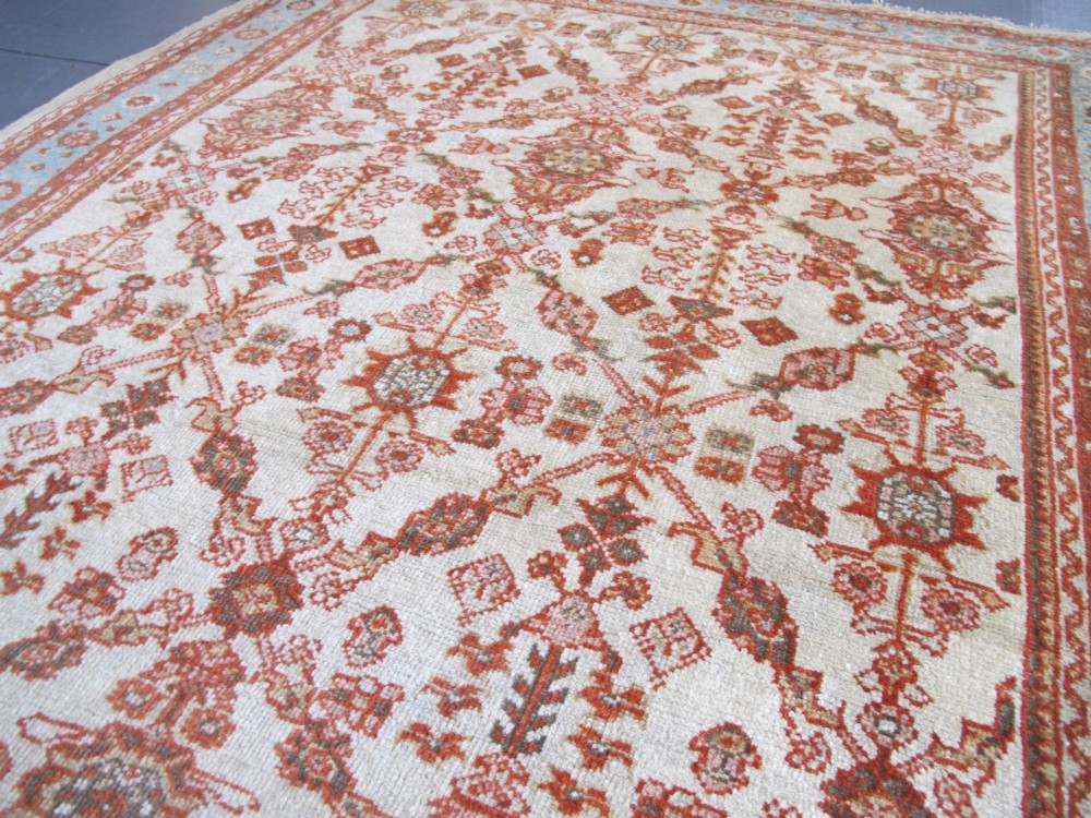 An antique Persian Ziegler wool rug featuring a repeating soft terracotta and light blue floral pattern across an ivory field, bordered by a decorative floral band. View X