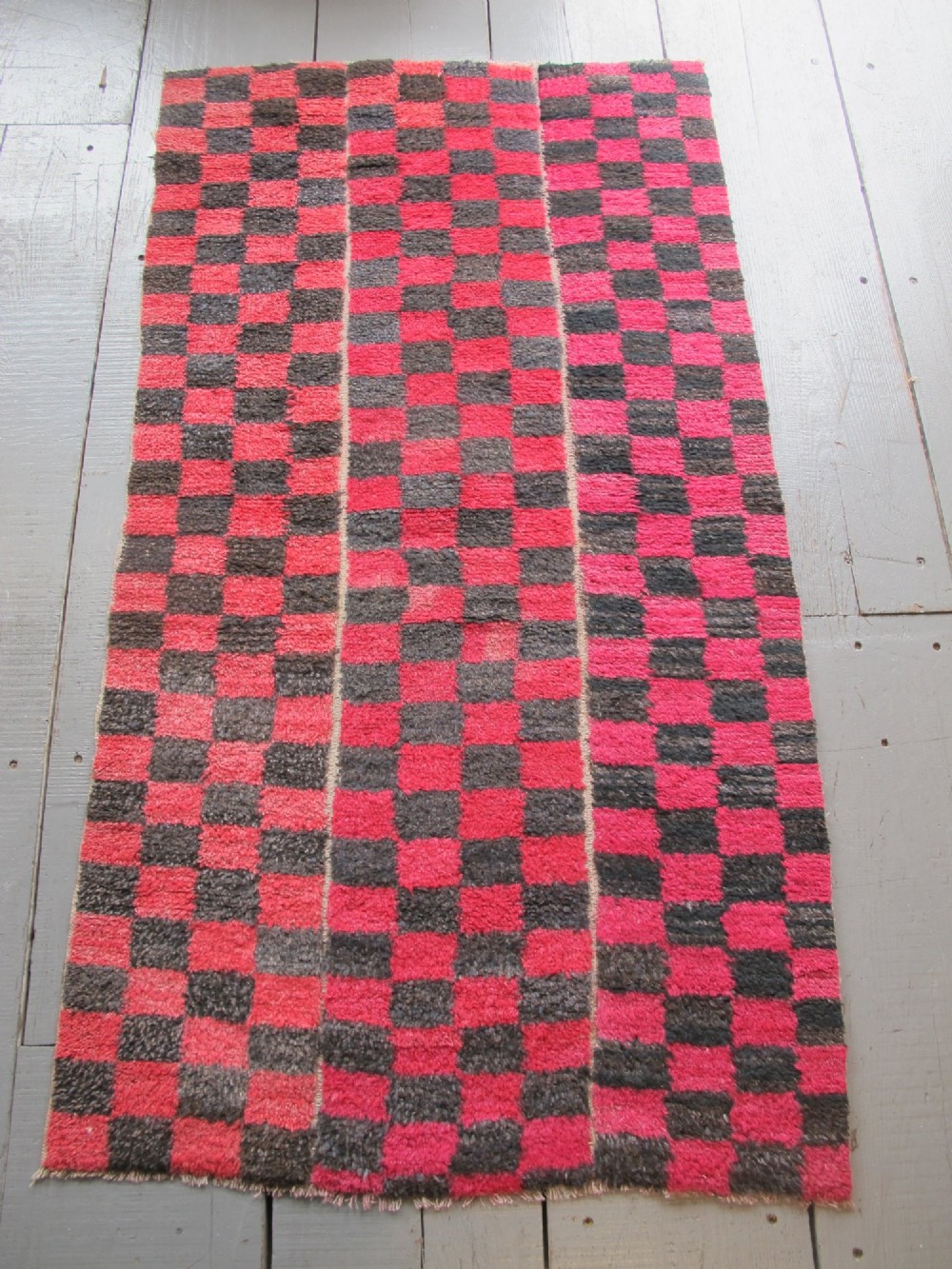 An antique Tibetan wool meditation rug featuring a three-panel chequerboard pattern in pink and dark grey.