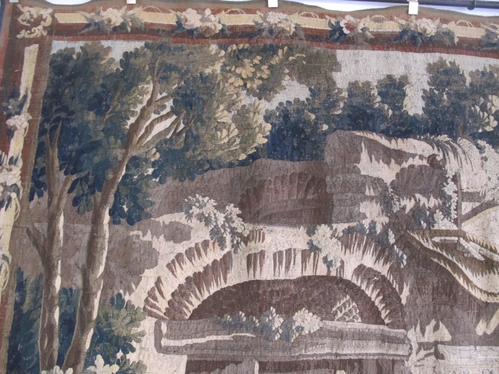 A large late 18th-century French woven tapestry portraying a pastoral scene with dancing figures, a stone building, and leafy trees enclosed within a decorative floral border. View VI