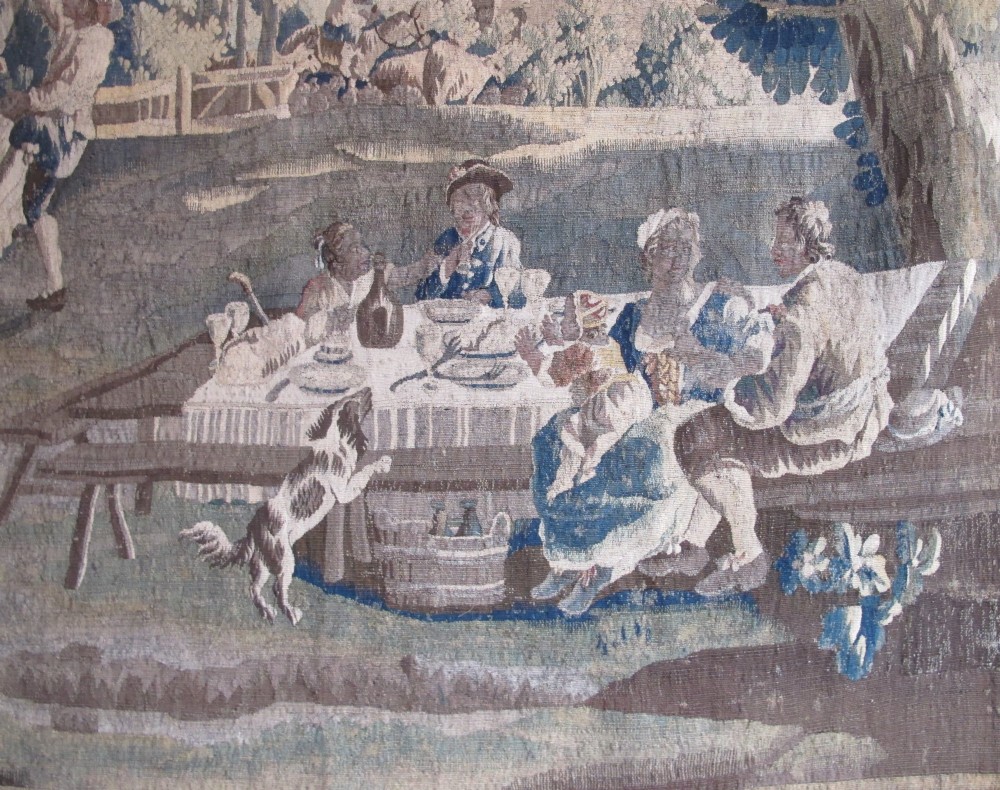 A large late 18th-century French woven tapestry portraying a pastoral scene with dancing figures, a stone building, and leafy trees enclosed within a decorative floral border. View X