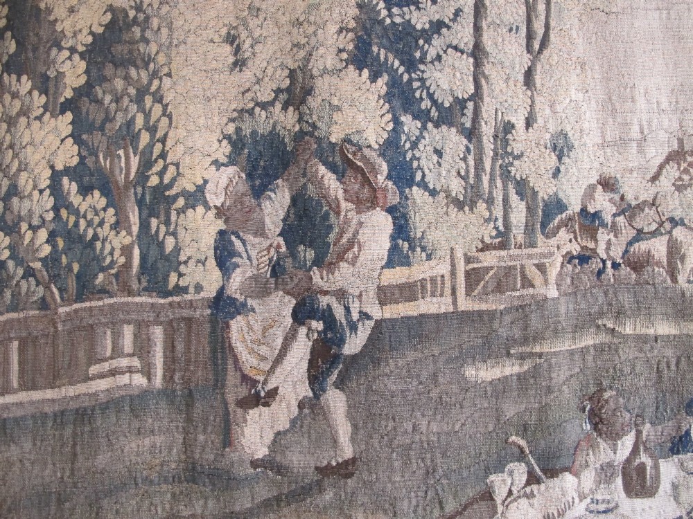 A large late 18th-century French woven tapestry portraying a pastoral scene with dancing figures, a stone building, and leafy trees enclosed within a decorative floral border. View XI