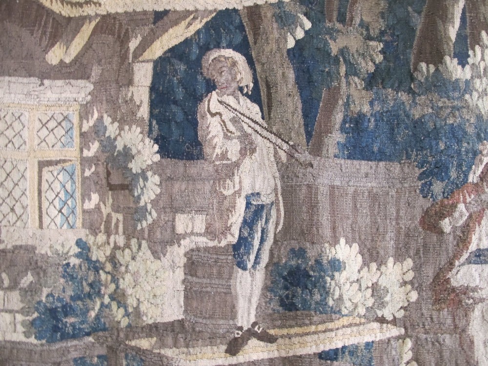 A large late 18th-century French woven tapestry portraying a pastoral scene with dancing figures, a stone building, and leafy trees enclosed within a decorative floral border. View XII