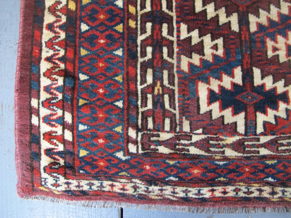 A pentagonal hand-woven wool textile featuring a red and cream geometric diamond lattice pattern with dark navy blue accents. View II