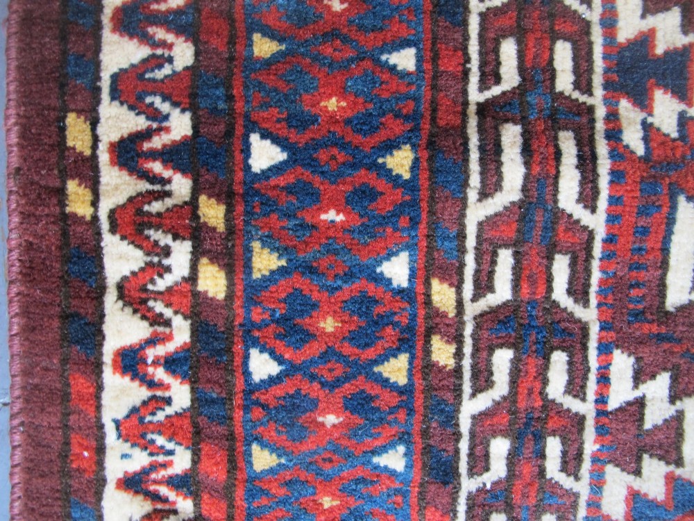 A pentagonal hand-woven wool textile featuring a red and cream geometric diamond lattice pattern with dark navy blue accents. View III