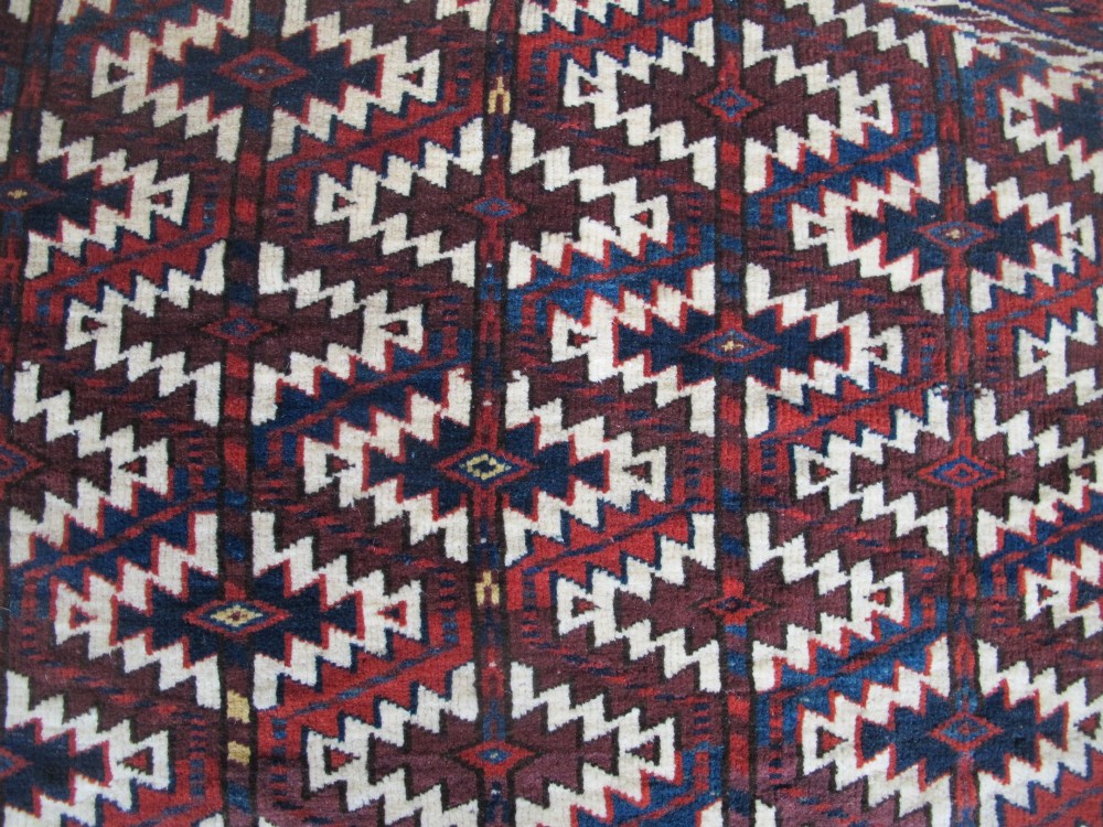 A pentagonal hand-woven wool textile featuring a red and cream geometric diamond lattice pattern with dark navy blue accents. View V