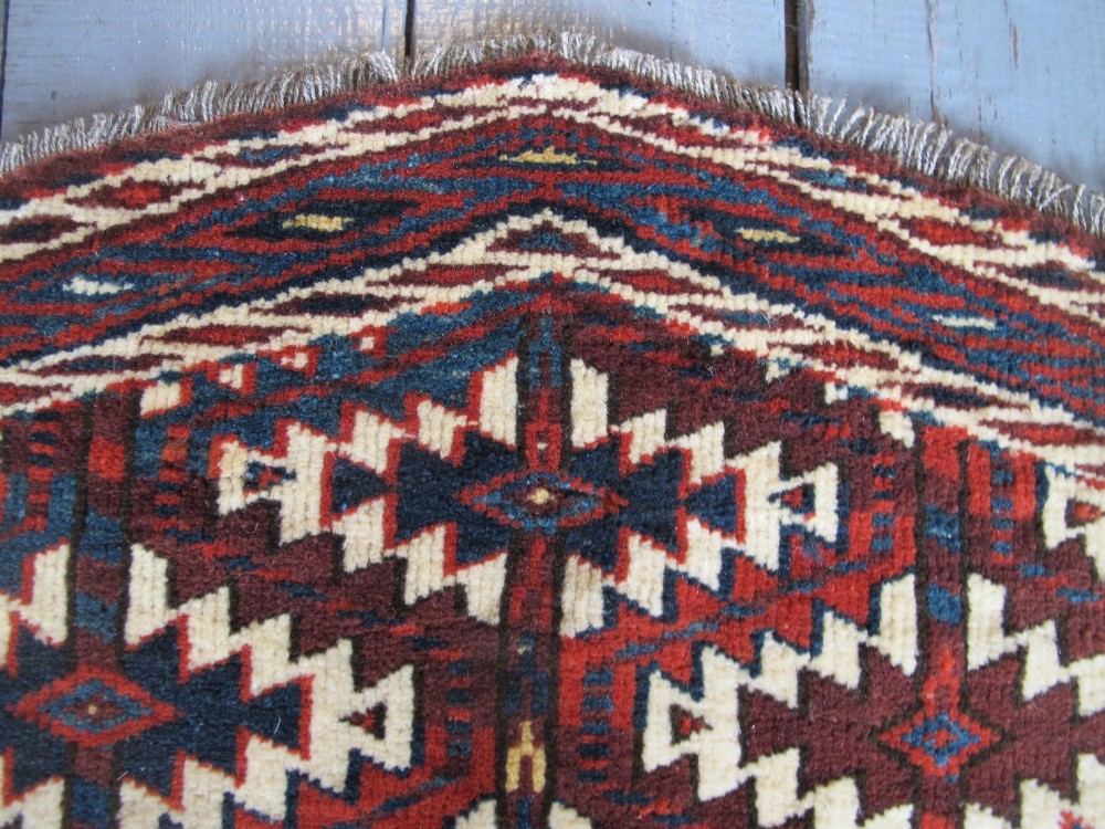 A pentagonal hand-woven wool textile featuring a red and cream geometric diamond lattice pattern with dark navy blue accents. View VII