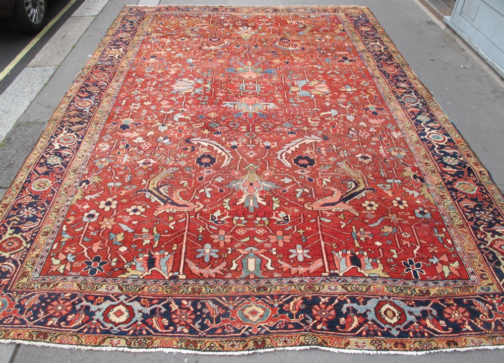 A large late 19th-century Heriz wool carpet featuring an all-over geometric floral motif in terracotta red and navy blue shades.