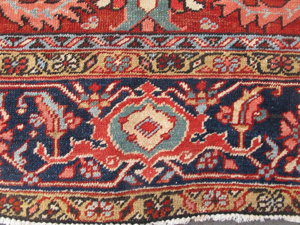 A large late 19th-century Heriz wool carpet featuring an all-over geometric floral motif in terracotta red and navy blue shades. View VI