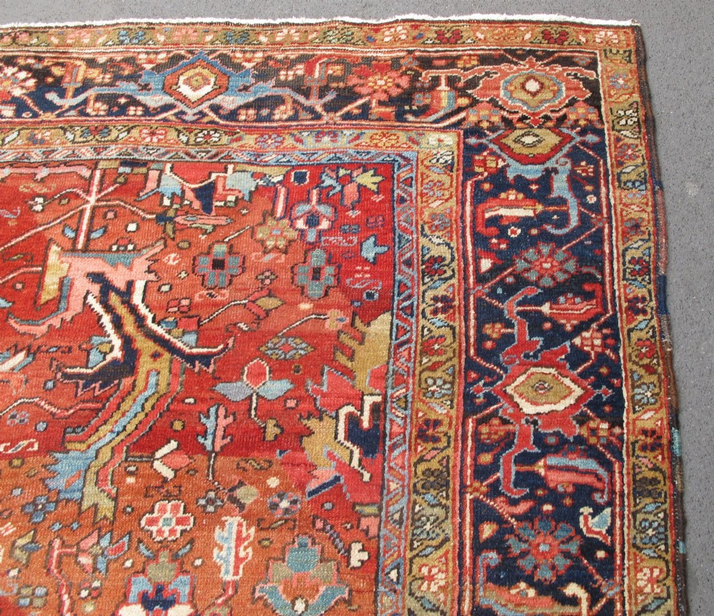 A large late 19th-century Heriz wool carpet featuring an all-over geometric floral motif in terracotta red and navy blue shades. View X