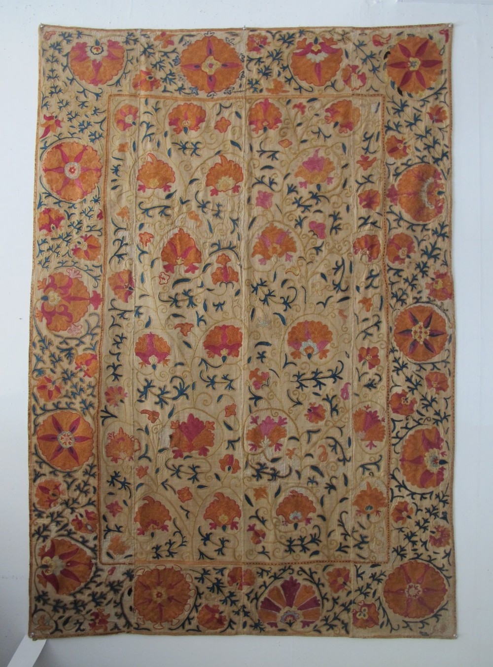 A rectangular hand-embroidered cream cotton textile decorated with orange, pink, and green silk floral roundels and scrolling vine borders.