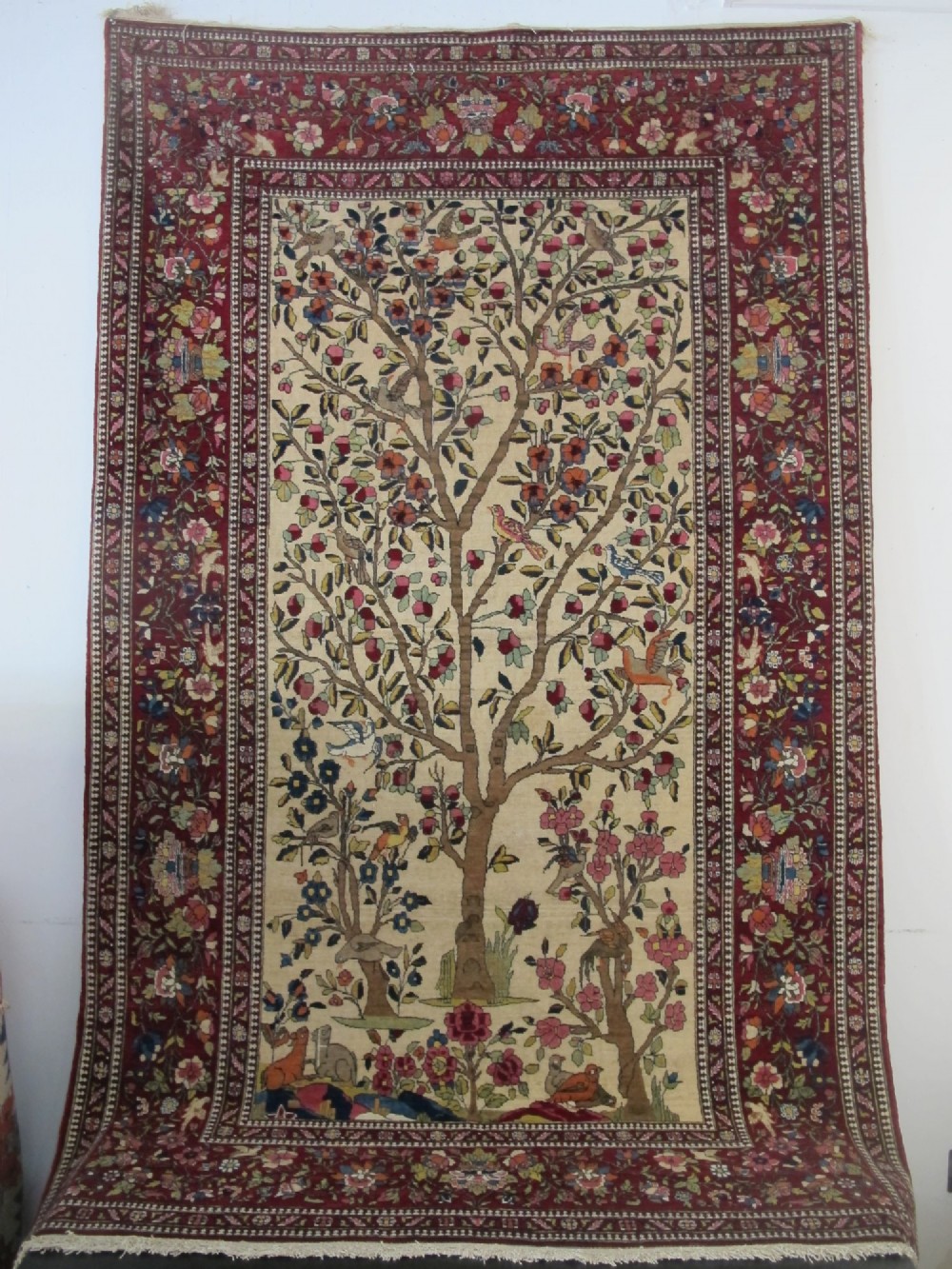An antique hand-knotted Persian Isfahan wool rug featuring a central cream field with a detailed Tree of Life and bird motifs, framed by a wide deep red floral border.