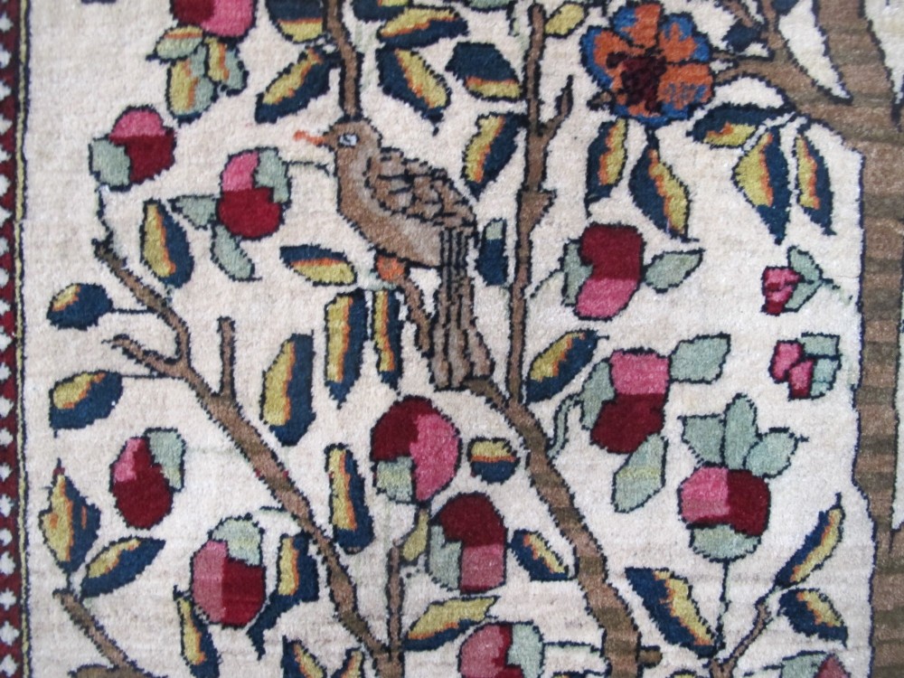 An antique hand-knotted Persian Isfahan wool rug featuring a central cream field with a detailed Tree of Life and bird motifs, framed by a wide deep red floral border. View V