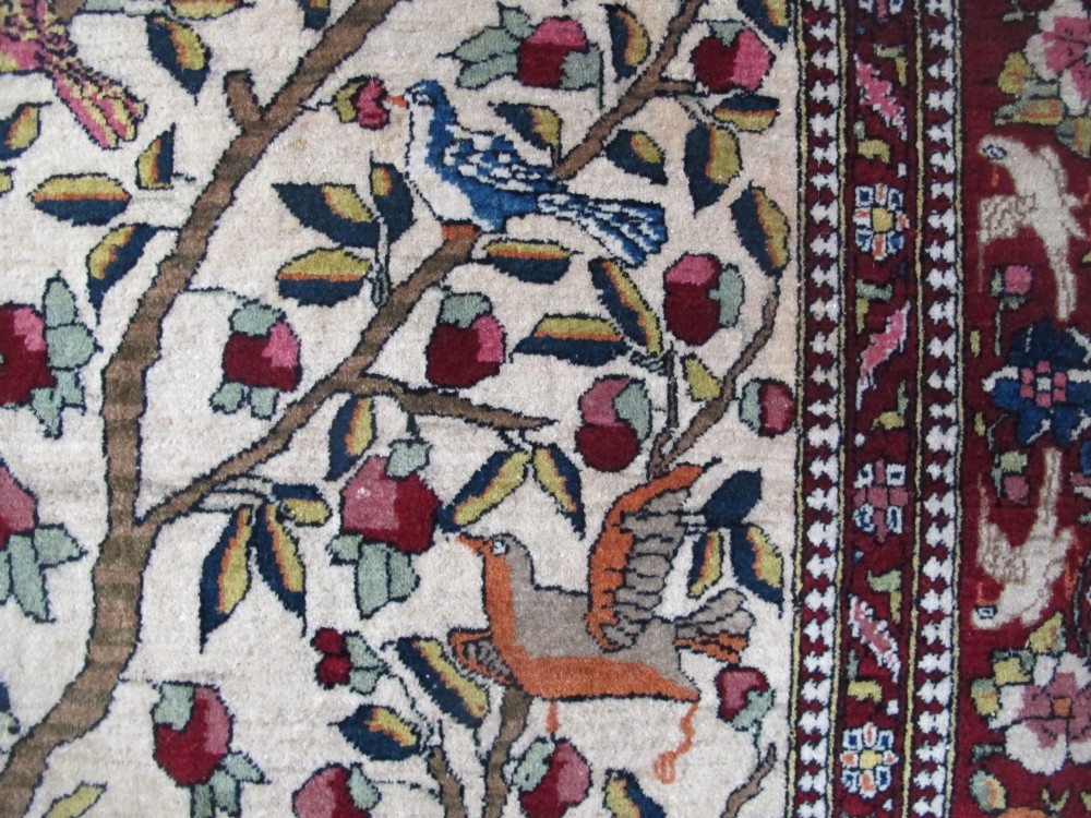 An antique hand-knotted Persian Isfahan wool rug featuring a central cream field with a detailed Tree of Life and bird motifs, framed by a wide deep red floral border. View VI