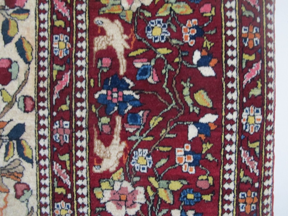 An antique hand-knotted Persian Isfahan wool rug featuring a central cream field with a detailed Tree of Life and bird motifs, framed by a wide deep red floral border. View VII