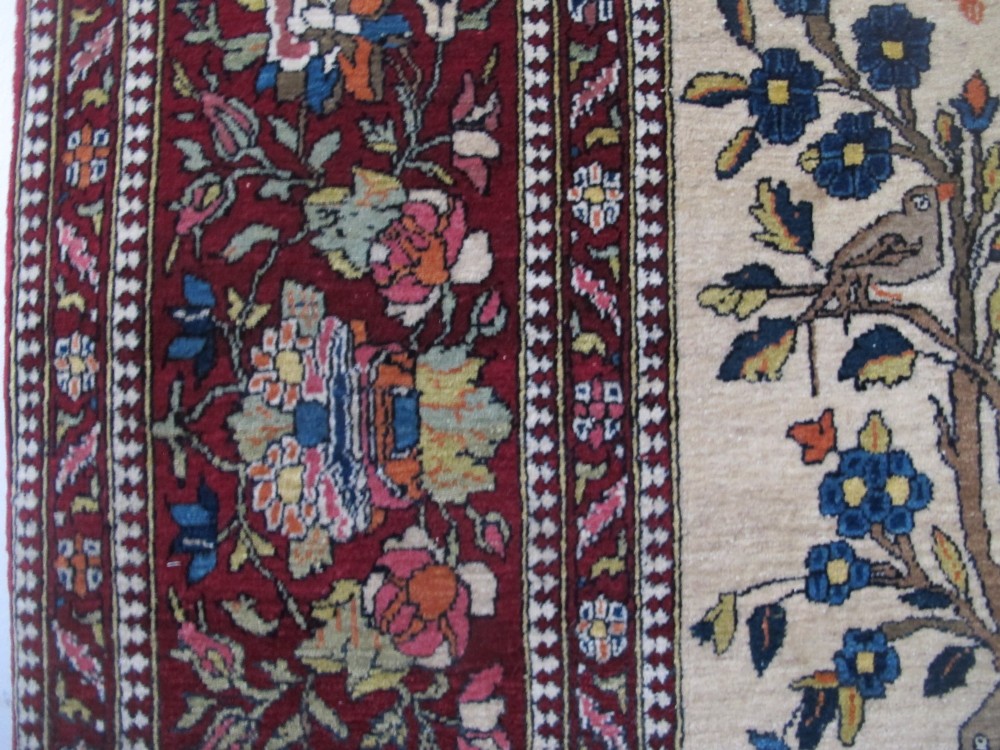 An antique hand-knotted Persian Isfahan wool rug featuring a central cream field with a detailed Tree of Life and bird motifs, framed by a wide deep red floral border. View IX