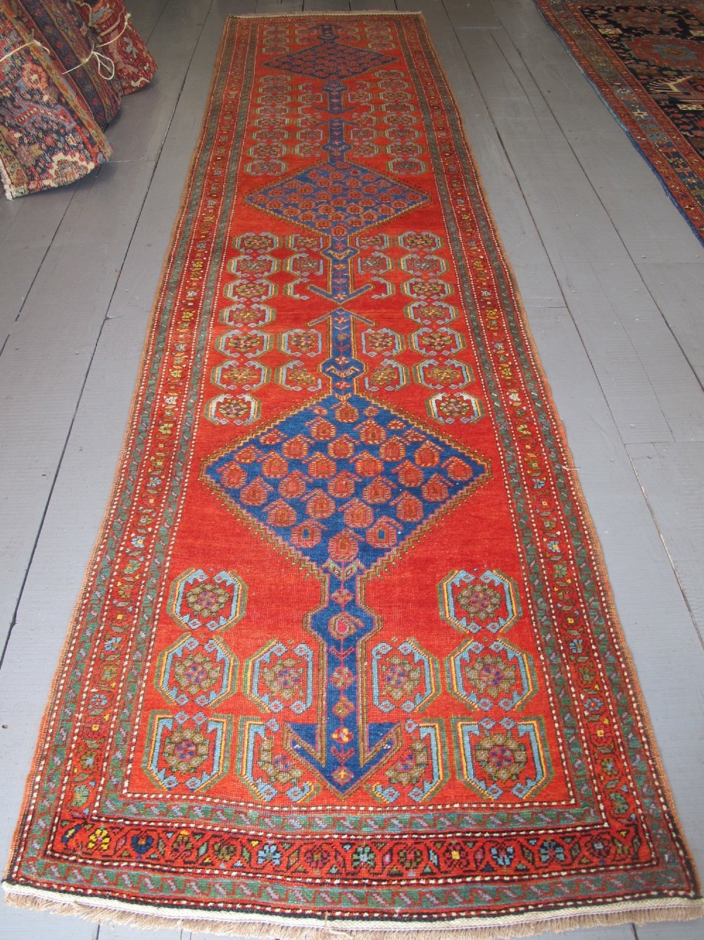 A long 19th-century Persian Bakshaish runner rug featuring central blue geometric diamond medallions on a bright red field with stylized floral borders.