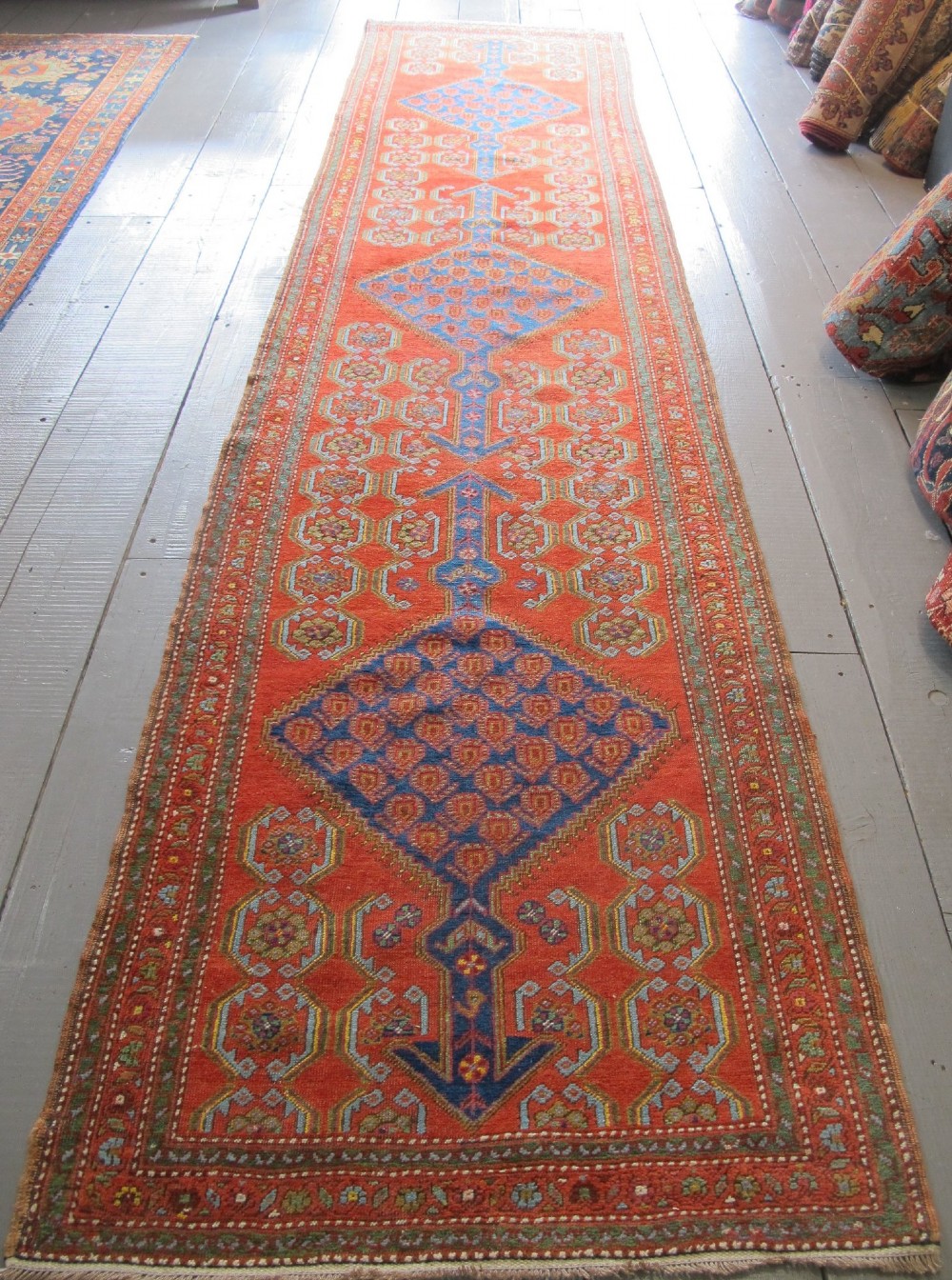 A long 19th-century Persian Bakshaish runner rug featuring central blue geometric diamond medallions on a bright red field with stylized floral borders. View II