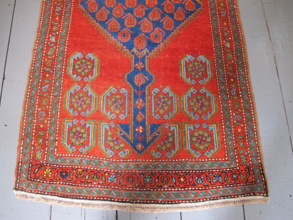 A long 19th-century Persian Bakshaish runner rug featuring central blue geometric diamond medallions on a bright red field with stylized floral borders. View III