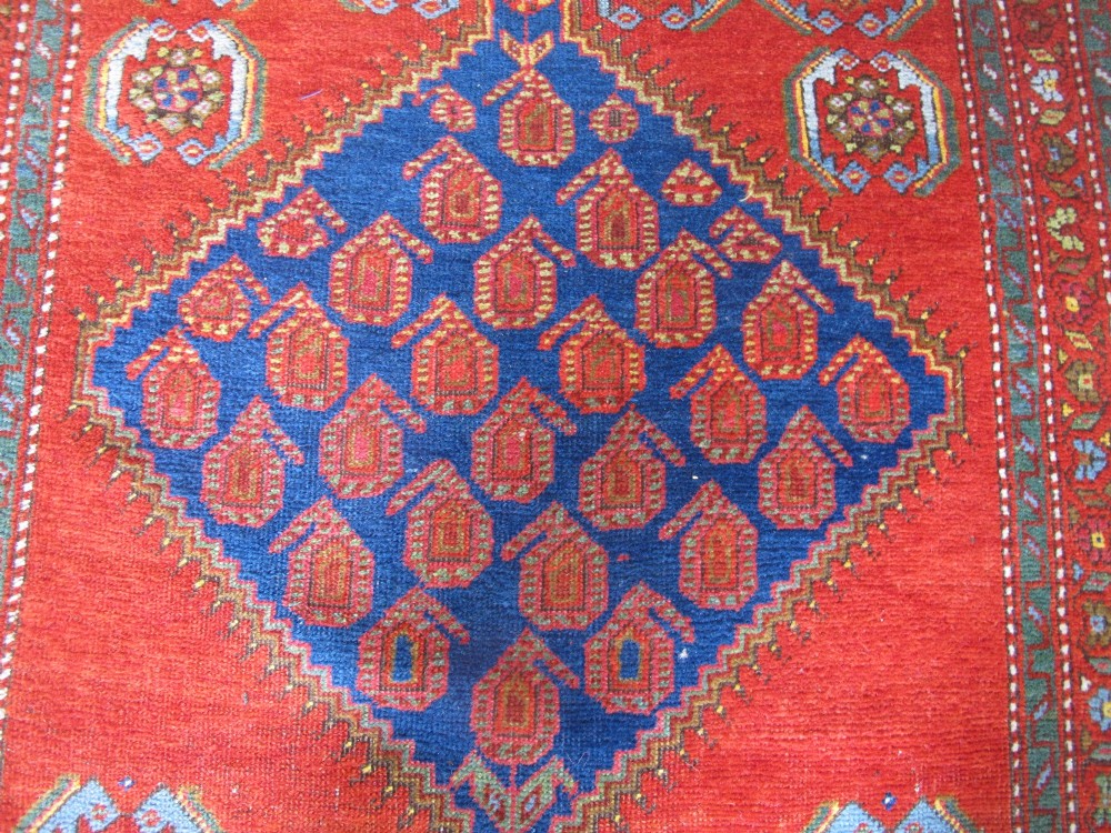 A long 19th-century Persian Bakshaish runner rug featuring central blue geometric diamond medallions on a bright red field with stylized floral borders. View IV