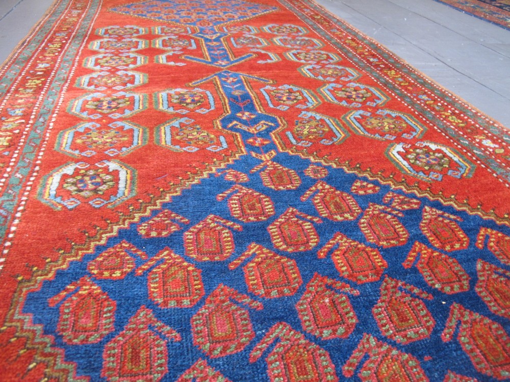 A long 19th-century Persian Bakshaish runner rug featuring central blue geometric diamond medallions on a bright red field with stylized floral borders. View V