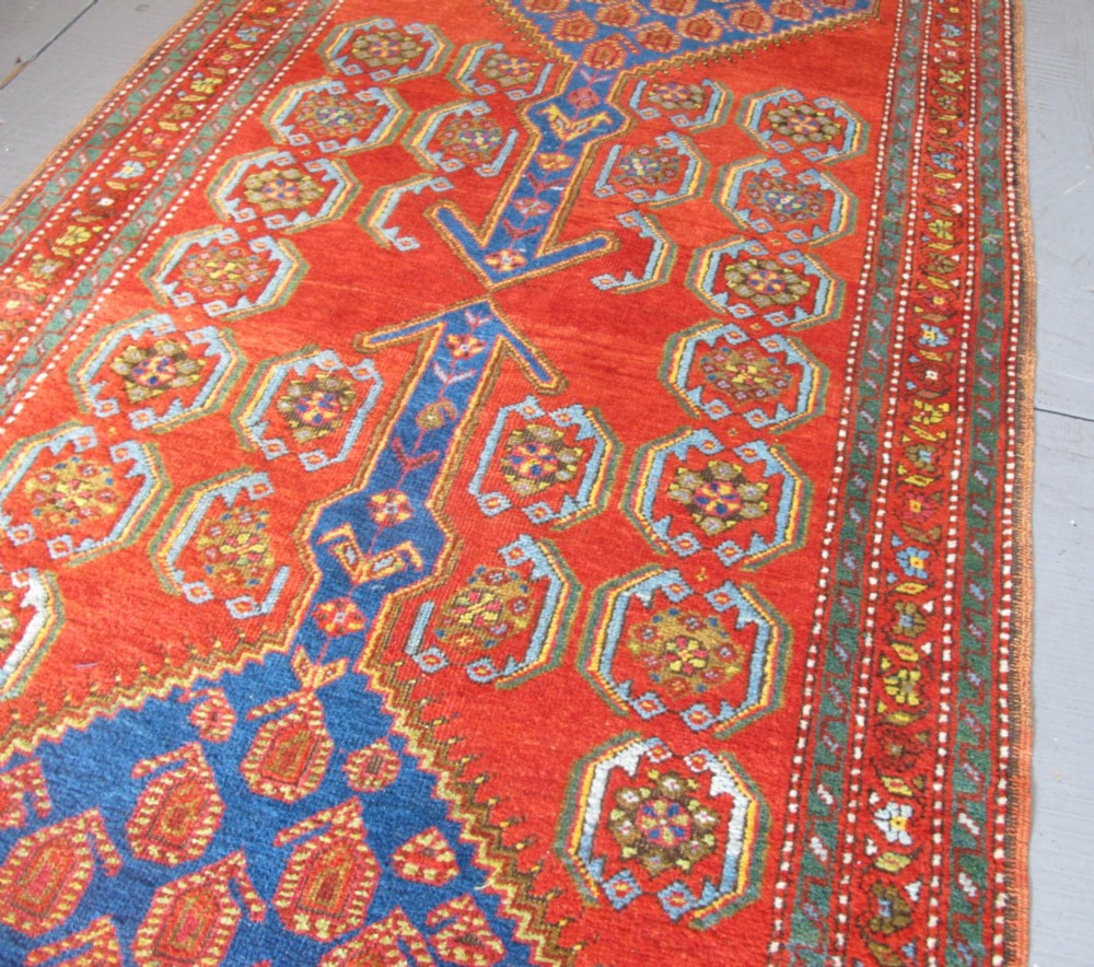 A long 19th-century Persian Bakshaish runner rug featuring central blue geometric diamond medallions on a bright red field with stylized floral borders. View VI