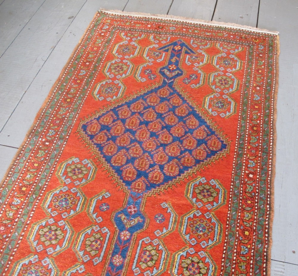 A long 19th-century Persian Bakshaish runner rug featuring central blue geometric diamond medallions on a bright red field with stylized floral borders. View IX
