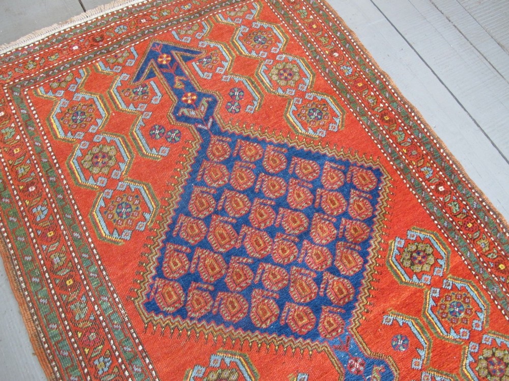 A long 19th-century Persian Bakshaish runner rug featuring central blue geometric diamond medallions on a bright red field with stylized floral borders. View X