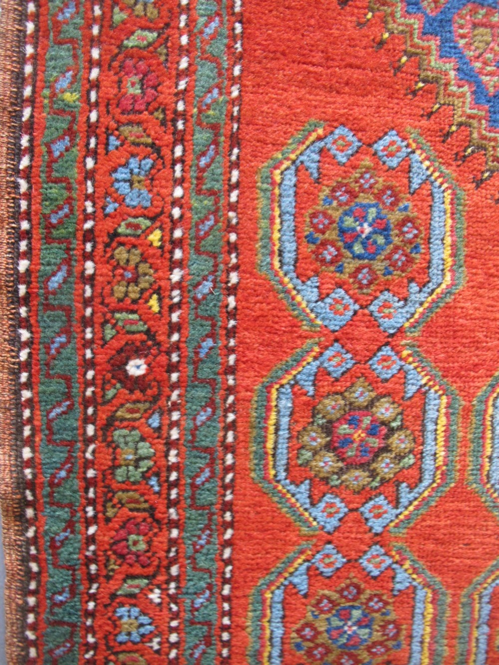 A long 19th-century Persian Bakshaish runner rug featuring central blue geometric diamond medallions on a bright red field with stylized floral borders. View XII