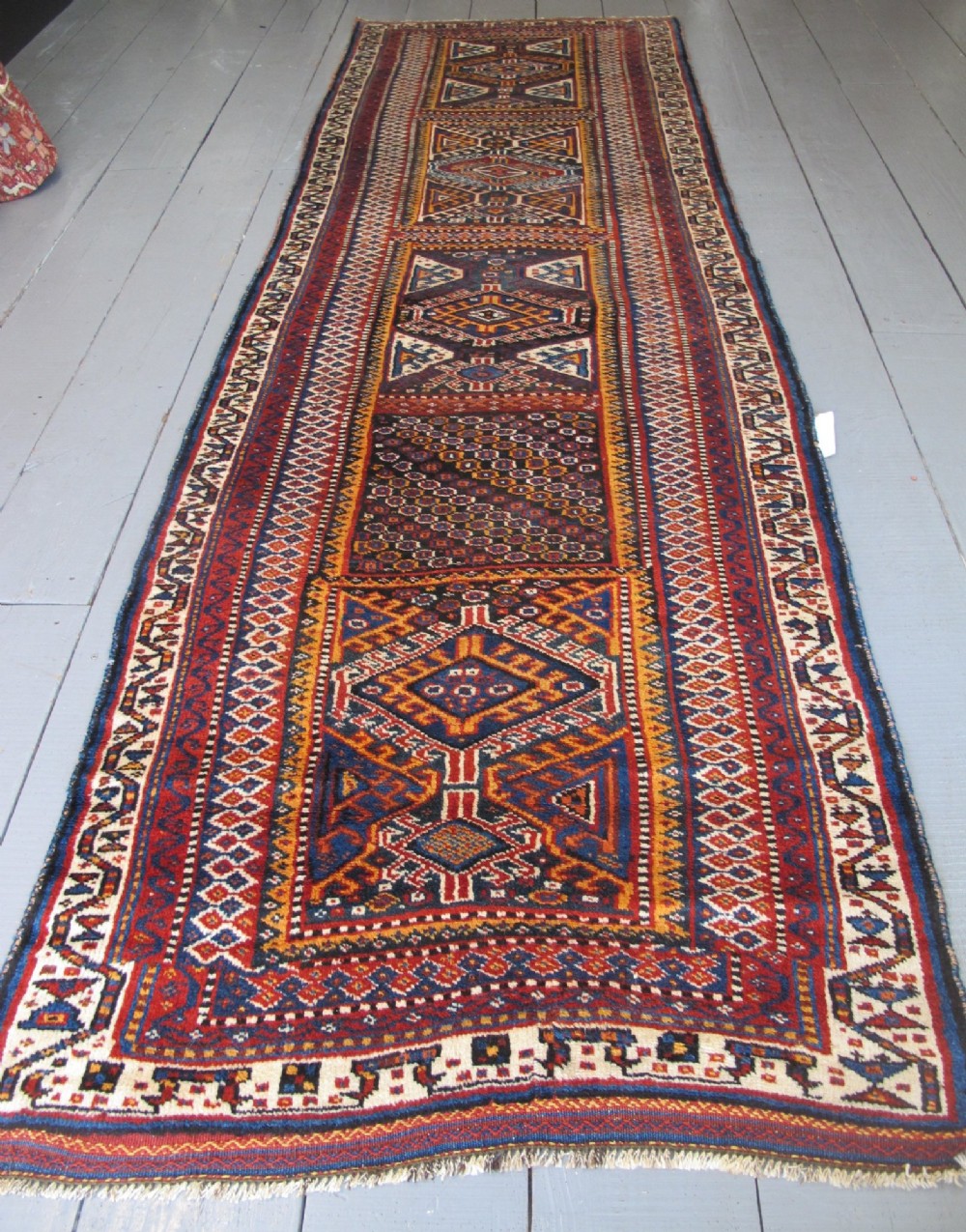 An antique late 19th-century Persian tribal runner rug with repeating geometric diamond medallions and layered borders in terracotta red, indigo blue, and ochre yellow. View II