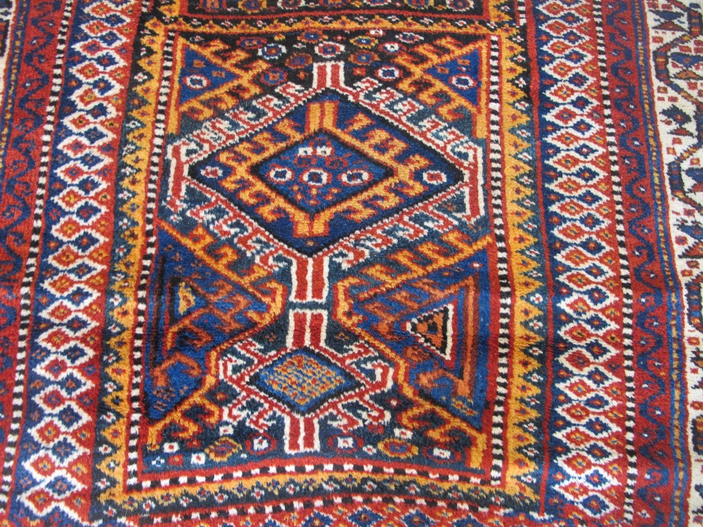 An antique late 19th-century Persian tribal runner rug with repeating geometric diamond medallions and layered borders in terracotta red, indigo blue, and ochre yellow. View III