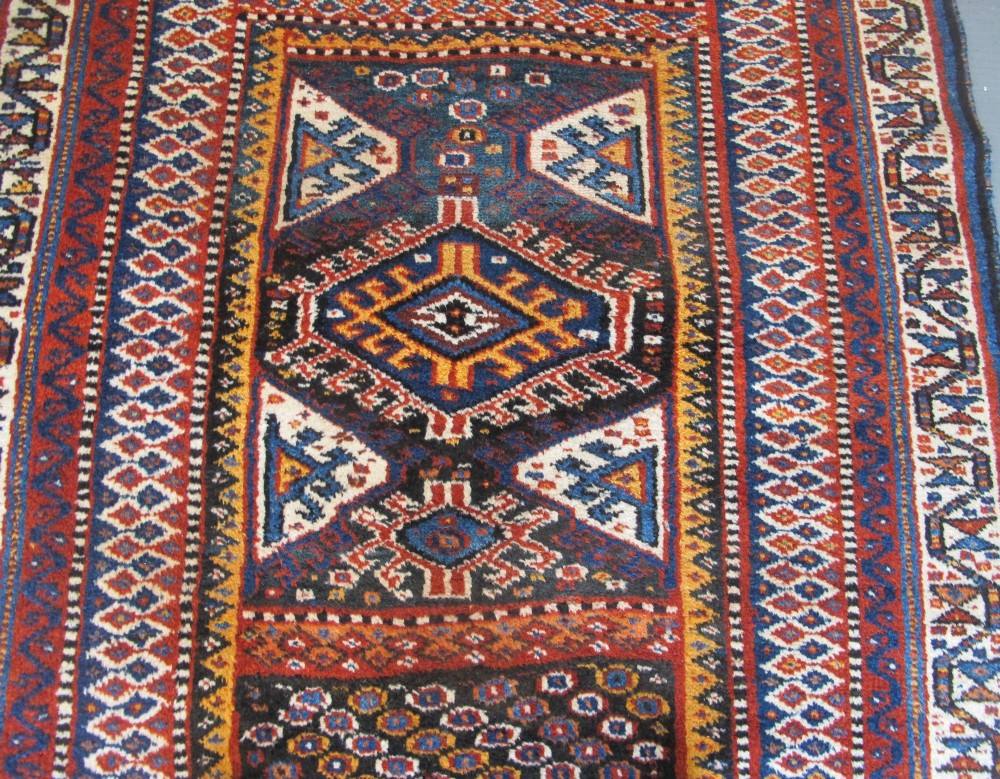An antique late 19th-century Persian tribal runner rug with repeating geometric diamond medallions and layered borders in terracotta red, indigo blue, and ochre yellow. View V