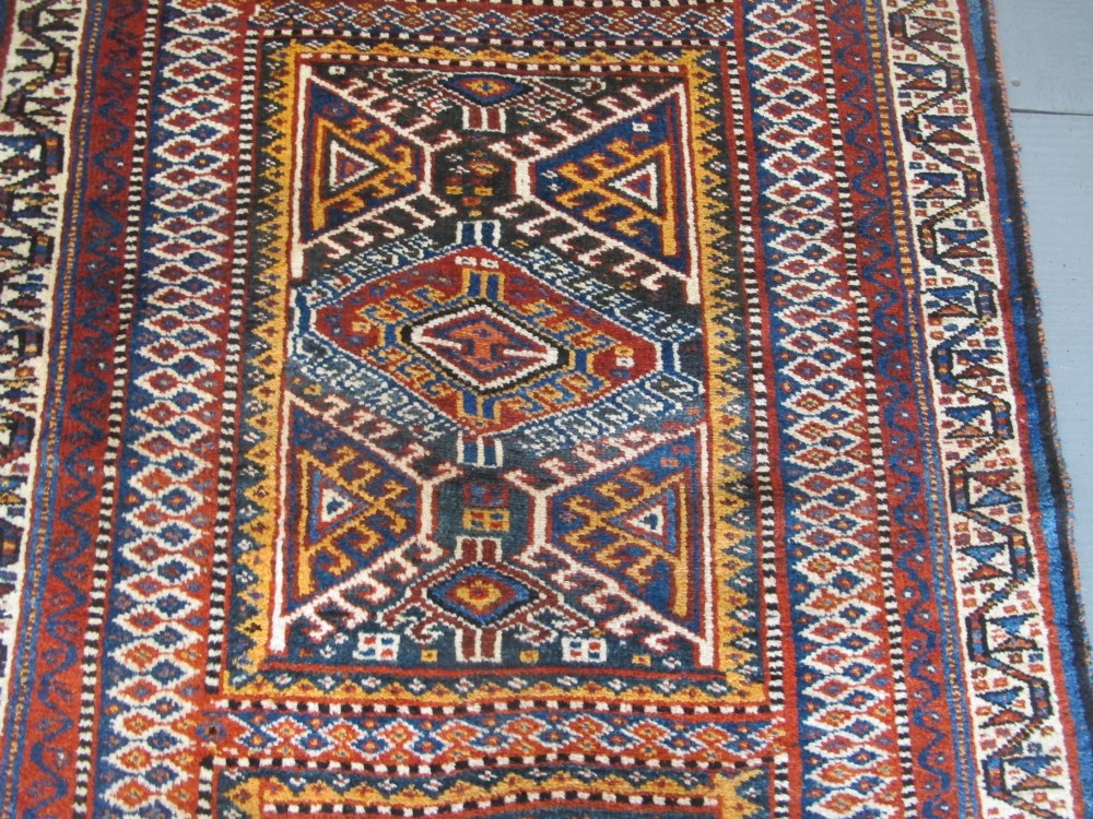 An antique late 19th-century Persian tribal runner rug with repeating geometric diamond medallions and layered borders in terracotta red, indigo blue, and ochre yellow. View VI
