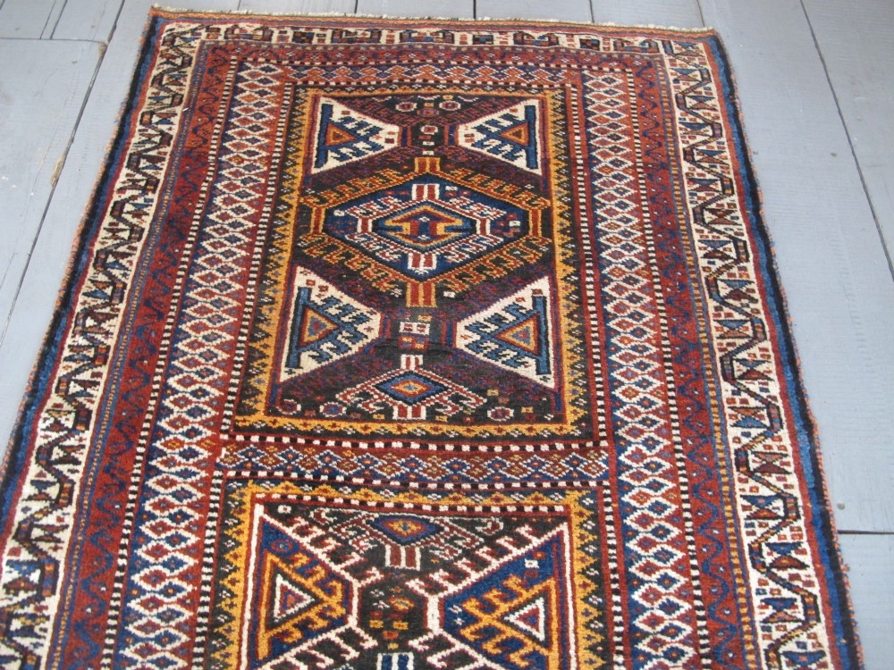 An antique late 19th-century Persian tribal runner rug with repeating geometric diamond medallions and layered borders in terracotta red, indigo blue, and ochre yellow. View VII