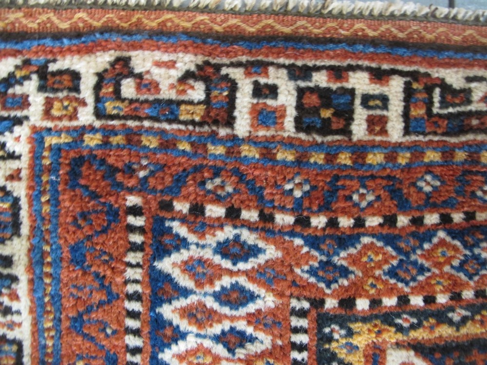 An antique late 19th-century Persian tribal runner rug with repeating geometric diamond medallions and layered borders in terracotta red, indigo blue, and ochre yellow. View IX