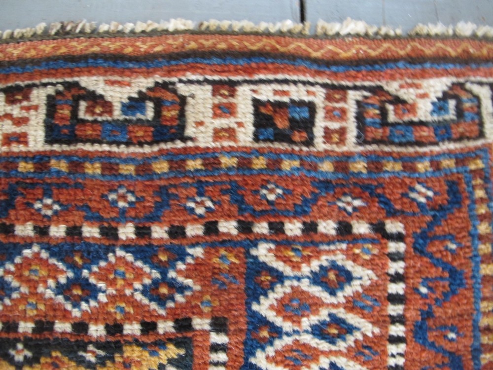 An antique late 19th-century Persian tribal runner rug with repeating geometric diamond medallions and layered borders in terracotta red, indigo blue, and ochre yellow. View X