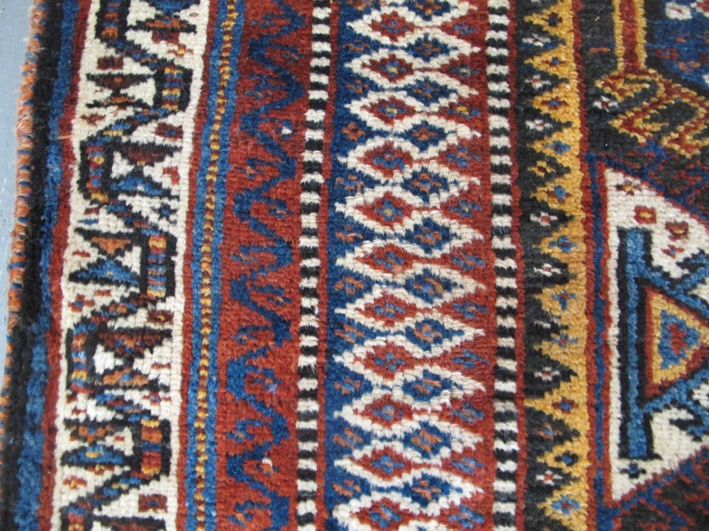 An antique late 19th-century Persian tribal runner rug with repeating geometric diamond medallions and layered borders in terracotta red, indigo blue, and ochre yellow. View XII