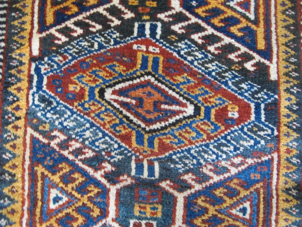 An antique late 19th-century Persian tribal runner rug with repeating geometric diamond medallions and layered borders in terracotta red, indigo blue, and ochre yellow. View XIII