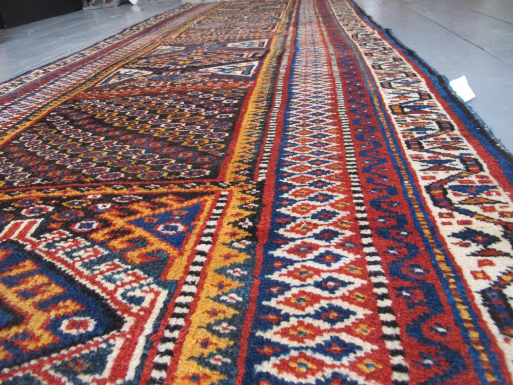 An antique late 19th-century Persian tribal runner rug with repeating geometric diamond medallions and layered borders in terracotta red, indigo blue, and ochre yellow. View XIV