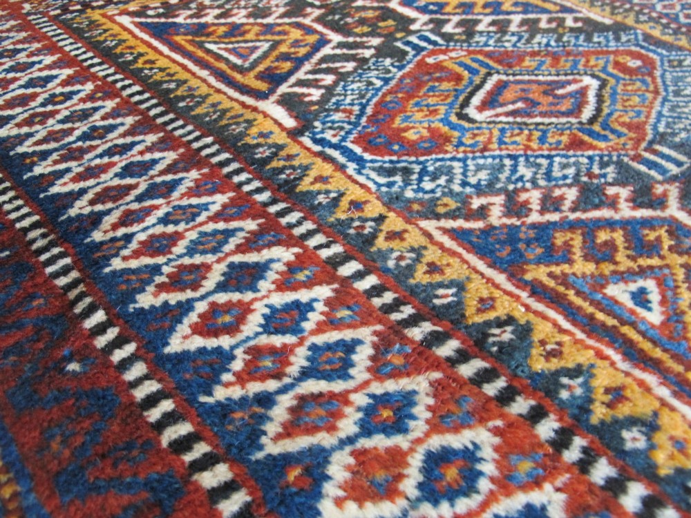 An antique late 19th-century Persian tribal runner rug with repeating geometric diamond medallions and layered borders in terracotta red, indigo blue, and ochre yellow. View XV