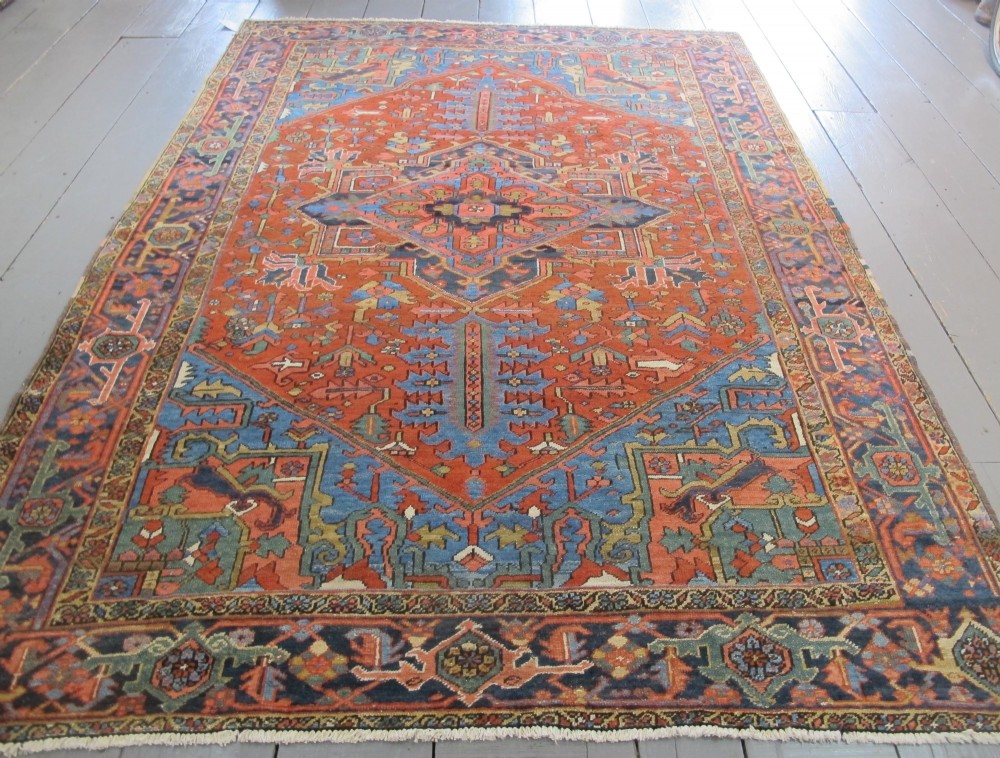 A hand-knotted late 19th-century Persian Heriz carpet featuring a central geometric medallion on a terracotta red field with blue spandrels and a multi-tiered border.