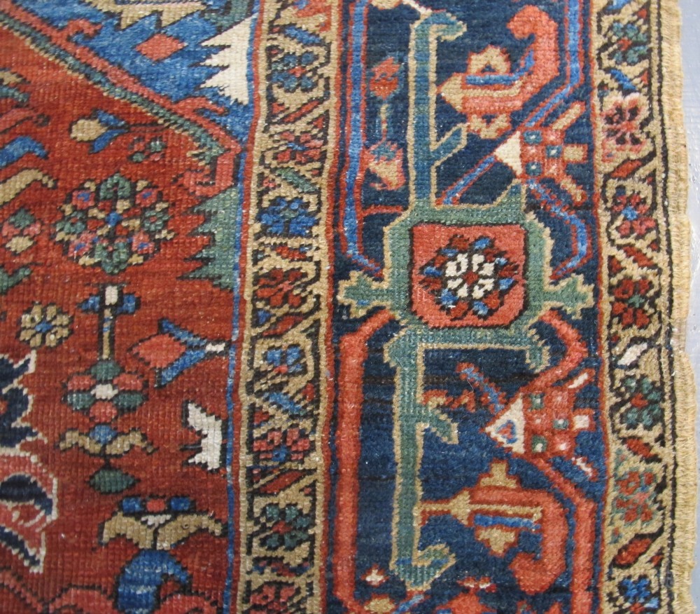 A hand-knotted late 19th-century Persian Heriz carpet featuring a central geometric medallion on a terracotta red field with blue spandrels and a multi-tiered border. View VI