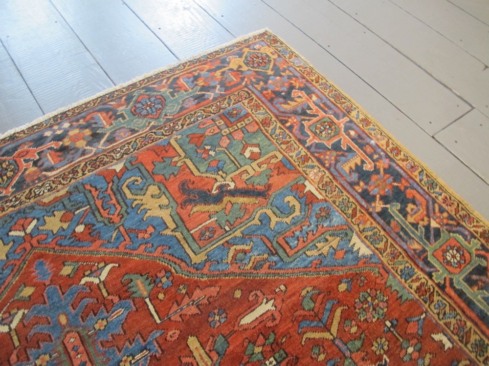 A hand-knotted late 19th-century Persian Heriz carpet featuring a central geometric medallion on a terracotta red field with blue spandrels and a multi-tiered border. View VII