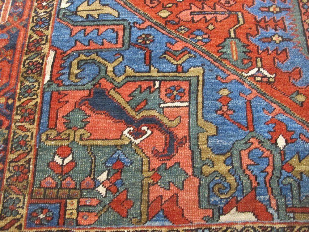 A hand-knotted late 19th-century Persian Heriz carpet featuring a central geometric medallion on a terracotta red field with blue spandrels and a multi-tiered border. View X