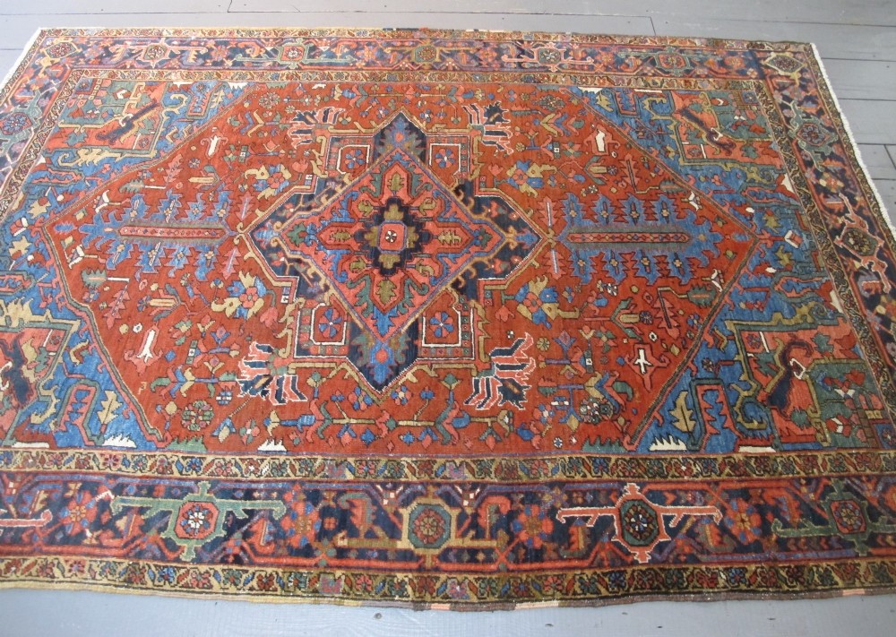 A hand-knotted late 19th-century Persian Heriz carpet featuring a central geometric medallion on a terracotta red field with blue spandrels and a multi-tiered border. View XV